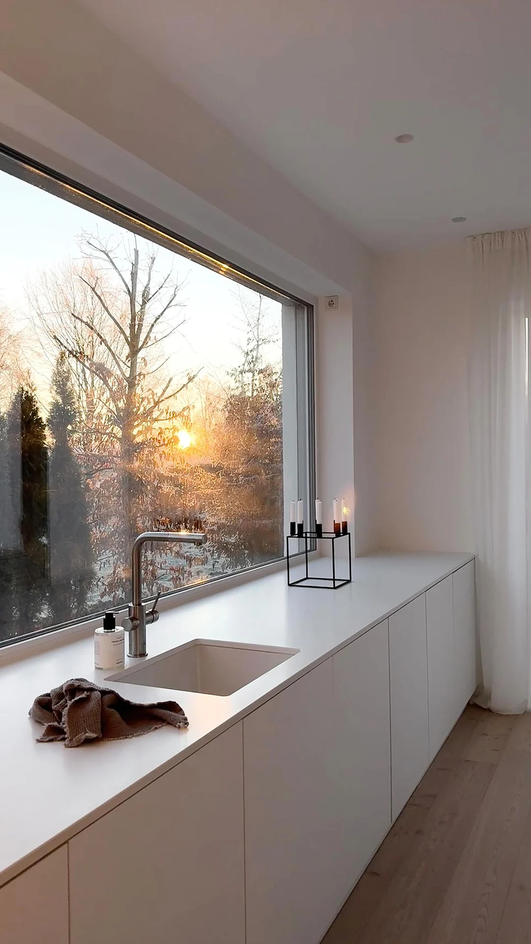 White handleless kitchen run with undermount sink in front of a large panoramic window White handleless kitchen run with undermount sink in front of a large panoramic window